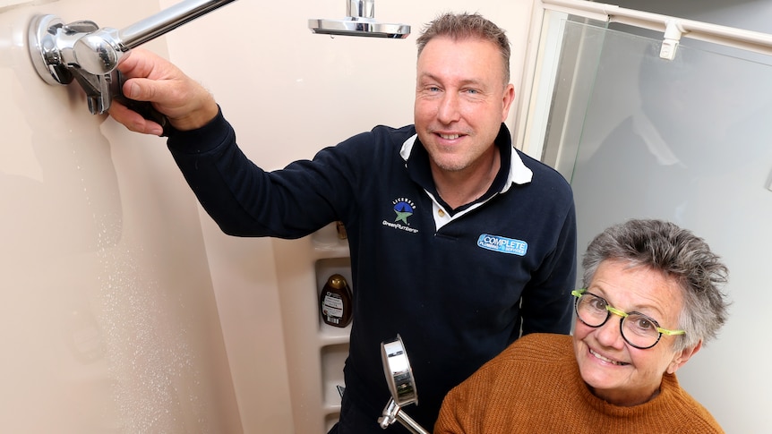 A plumber with newly installed showerhead next to retiree woman holding old showerhead