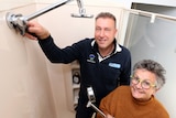 A plumber with newly installed showerhead next to retiree woman holding old showerhead