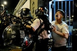 A bleeding man is taken away by policemen outside Kwai Chung police station in Hong Kong, the police are wearing riot gear.