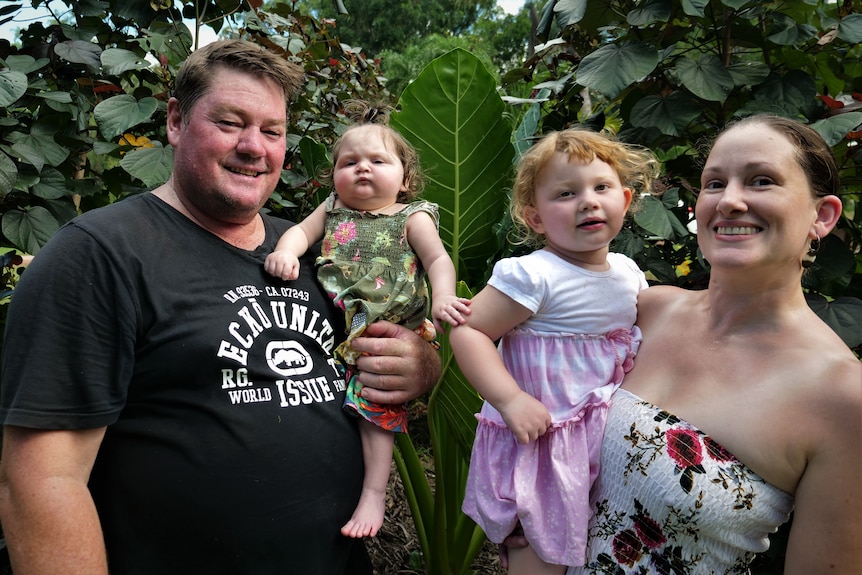 A family of four in a garden. Mum and dad are holding two young girls.