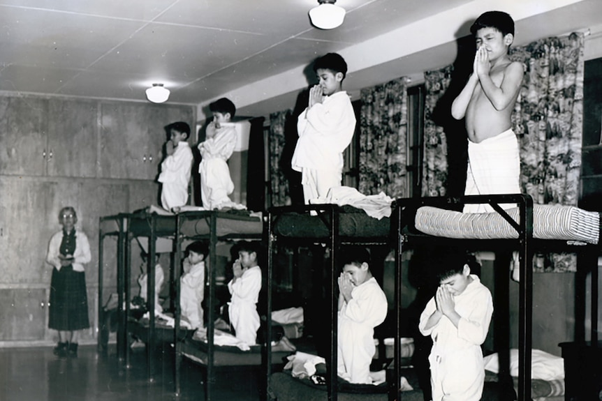 A group of young boys kneels in prayers on bunk beds