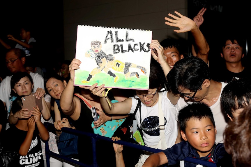 Fans hold up an All Blacks sign as they greet the arrival of the men's New Zealand rugby union team.