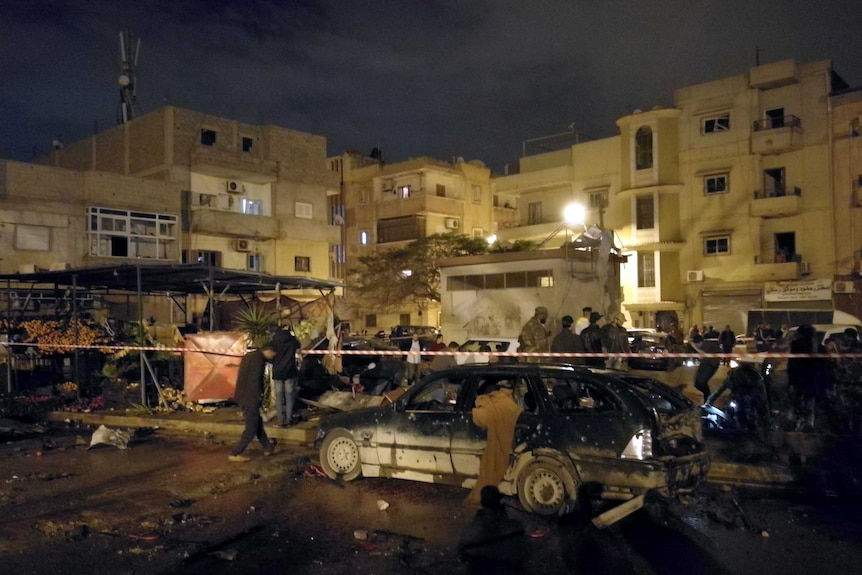 People walk between blown out cars and debris in the aftermath of a twin car bombing in Benghazi.
