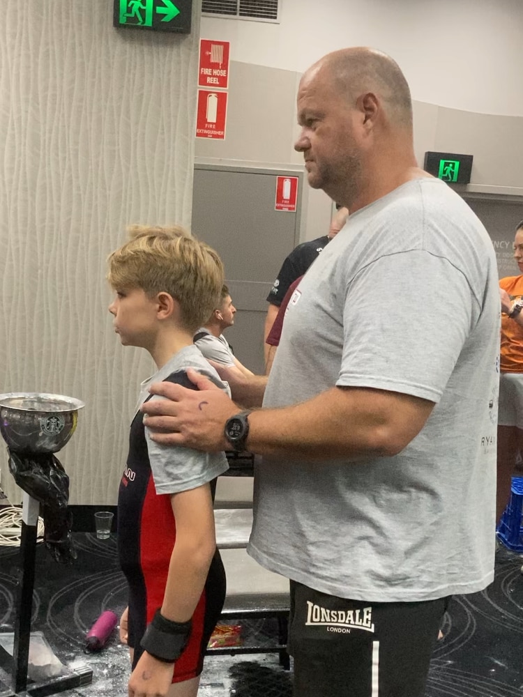 A young boy with his father standing behind him resting his hands on his shoulders