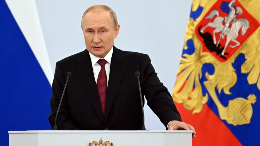 Vladimir Putin makes speech behind white podium.