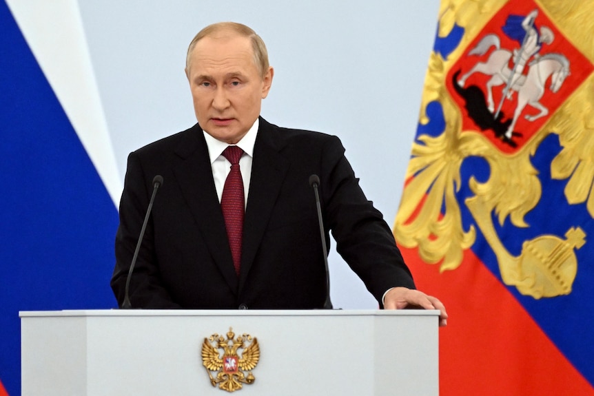 Vladimir Putin makes speech behind white podium.