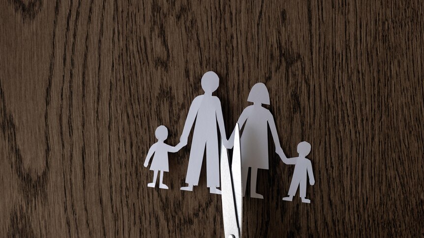 paper cut-out of father, mother and two children with a pair of scissors cutting through the middle on a woodgrain background