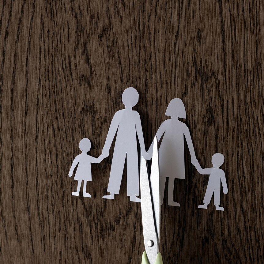 paper cut-out of father, mother and two children with a pair of scissors cutting through the middle on a woodgrain background