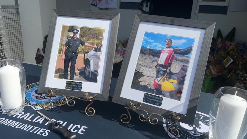Two framed pictures on a table in front of a police station with flowers on the door step.