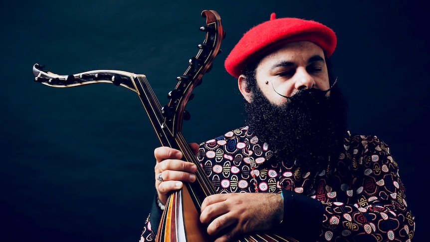 Joseph Tawadros in red beret and colourful shirt with big, bushy black beard and curled moustache with wings upwards