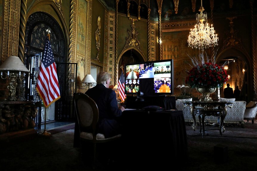 Donald Trump inside a very large gilded room in front of a TV