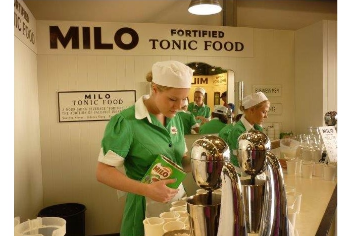 Two young women making milkshakes under a Milo Fortified Tonic Food sign.