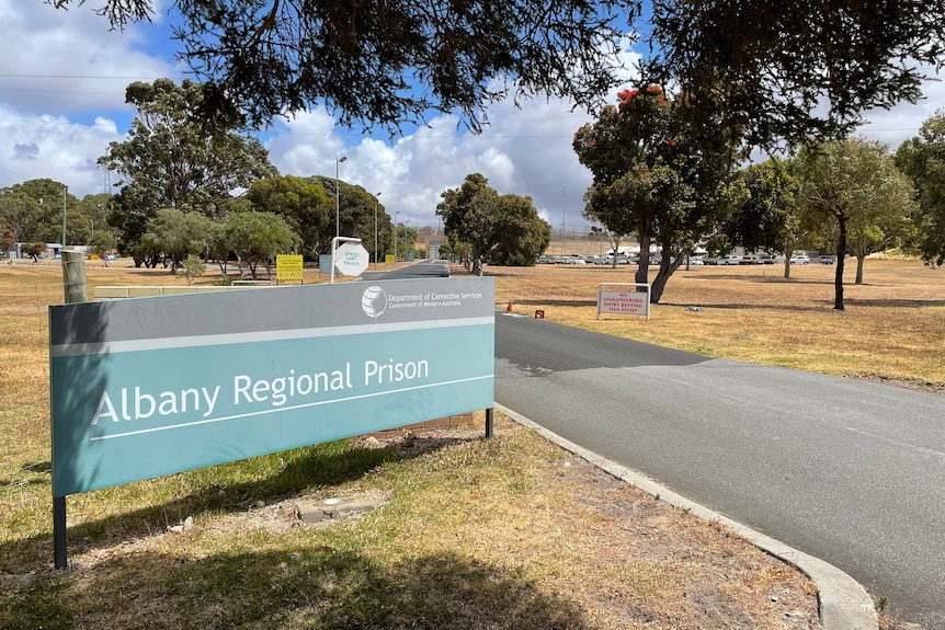 A sign at the entrance to Albany Regional Prison, to the left of a bitumen road.