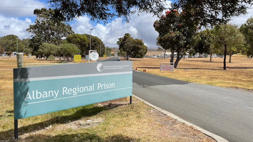 A sign at the entrance to Albany Regional Prison, to the left of a bitumen road.