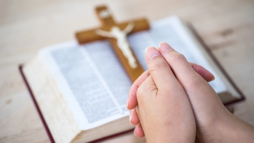 A Bible, a cross, and hands held in prayer