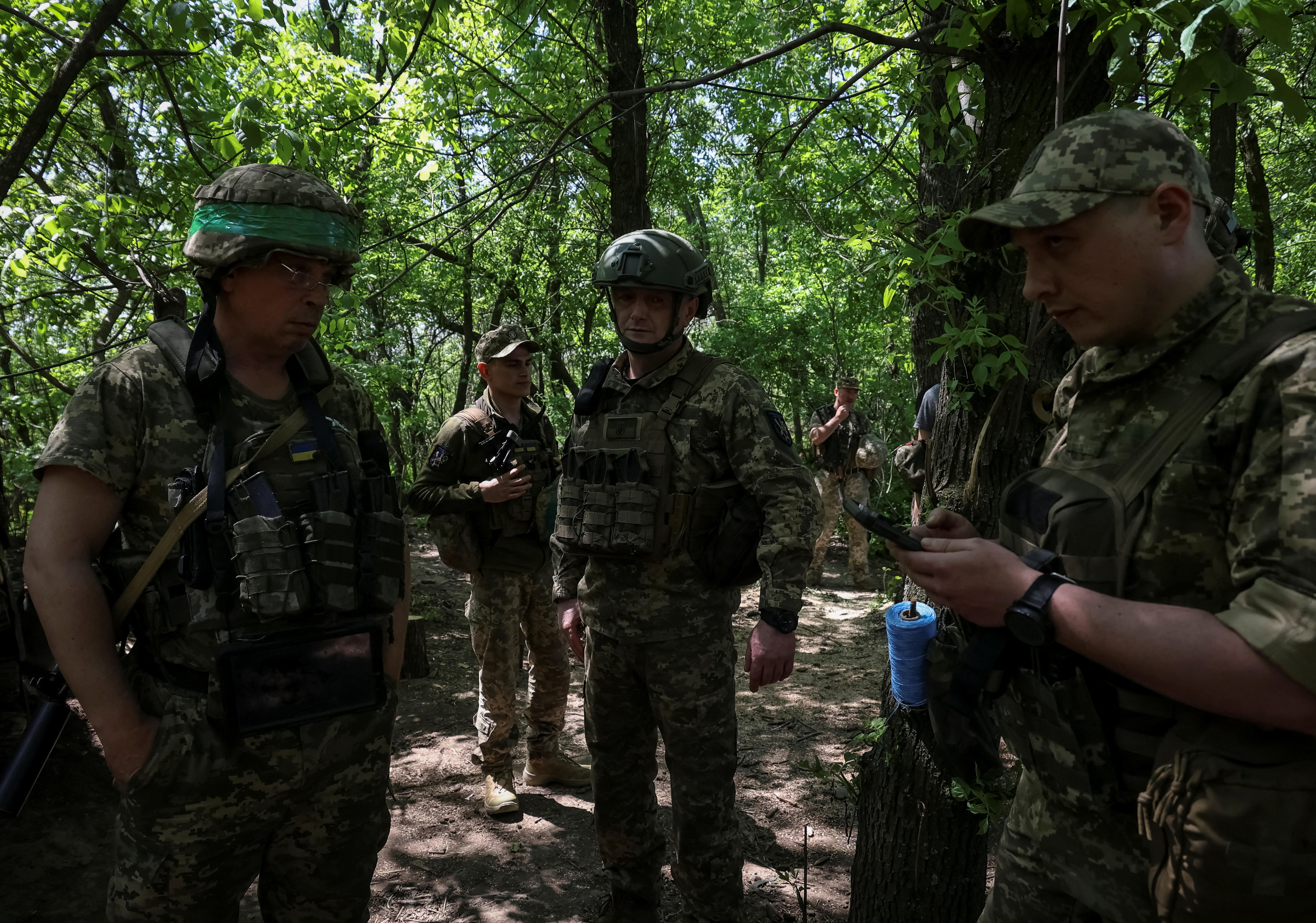 Ukrainian service members stand together inside forrested area.