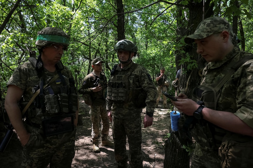 Ukrainian service members stand together inside forrested area.