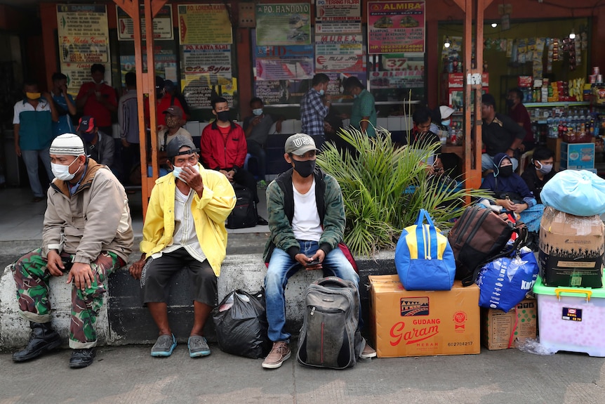 People sit with their belongings at a bus station