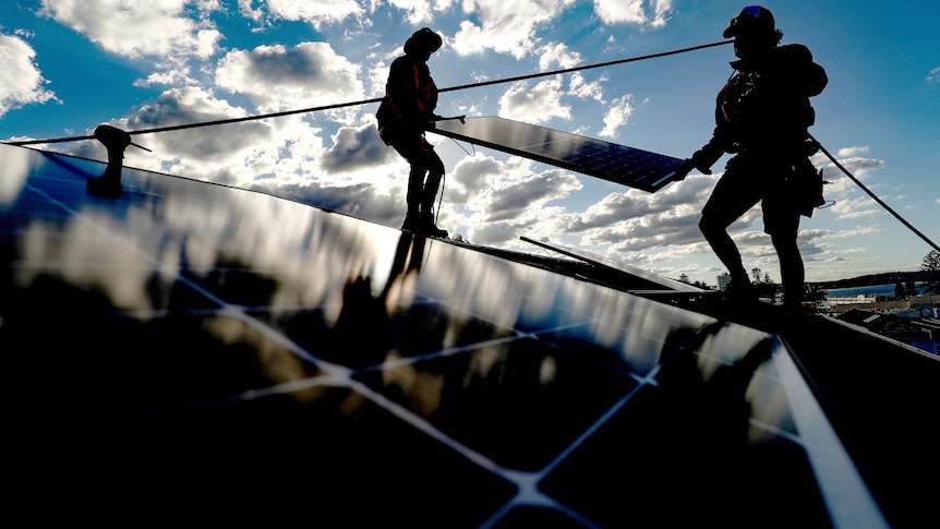 Silhouettes of two workers carrying a solar panel on a rooftop