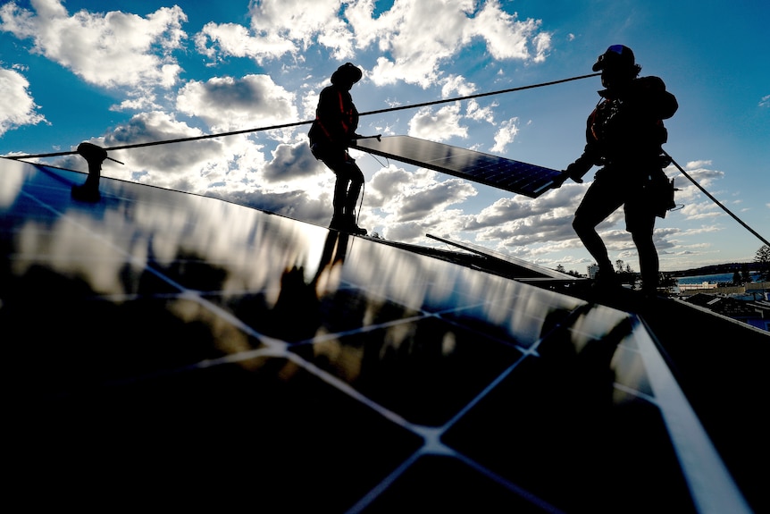 Silhouettes of two workers carrying a solar panel on a rooftop
