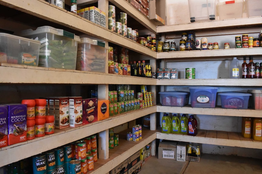 A pantry with five wooden shelves is stocked with items.