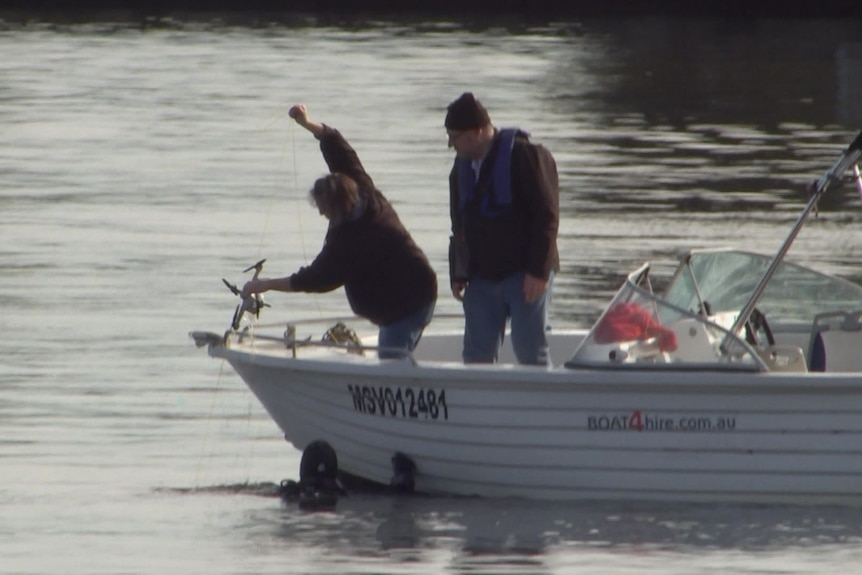 A person in a boat lifting a drone out of the water.