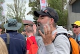A man with a large beard and baseball cap holds his hands in the air as he voices his displeasure outside the gates to the AGP.