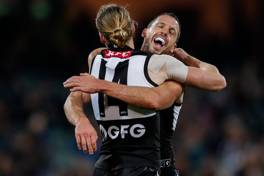 Two Port Adelaide AFL players embrace as they celebrate a goal.