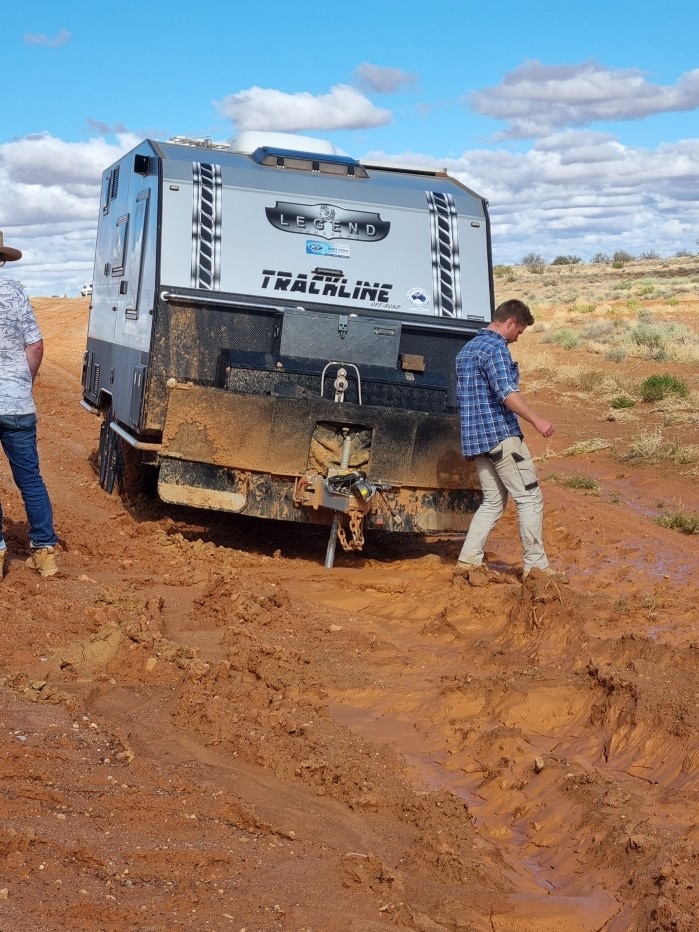 A silver-coloured caravan bogged on the side of a dirt road.