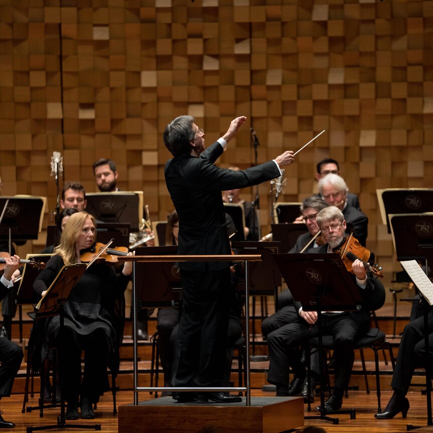 Conductor Eivind Aadland stands on a podum conducting the orchestra