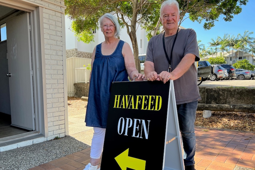 A woman and a man stand in front of a sign saying HavaFeed