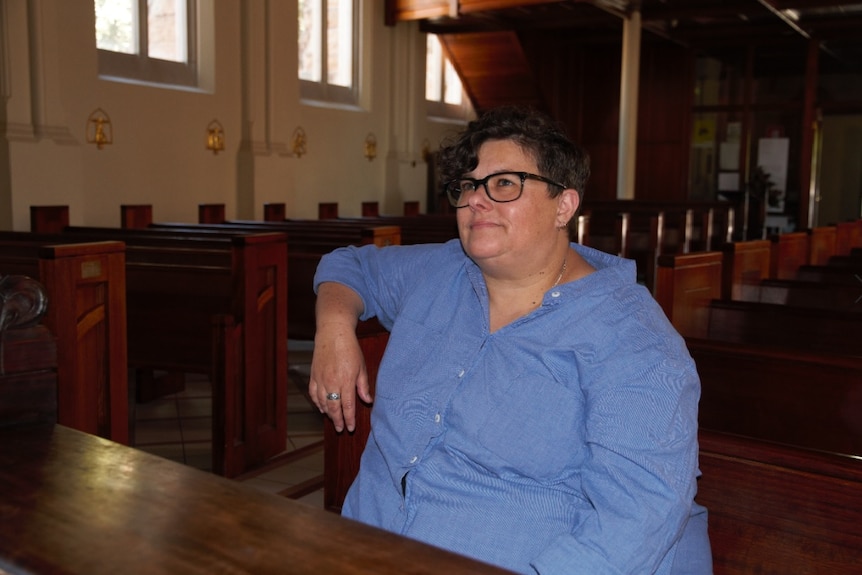 A woman sits in a church pew looking ahead past the camera.
