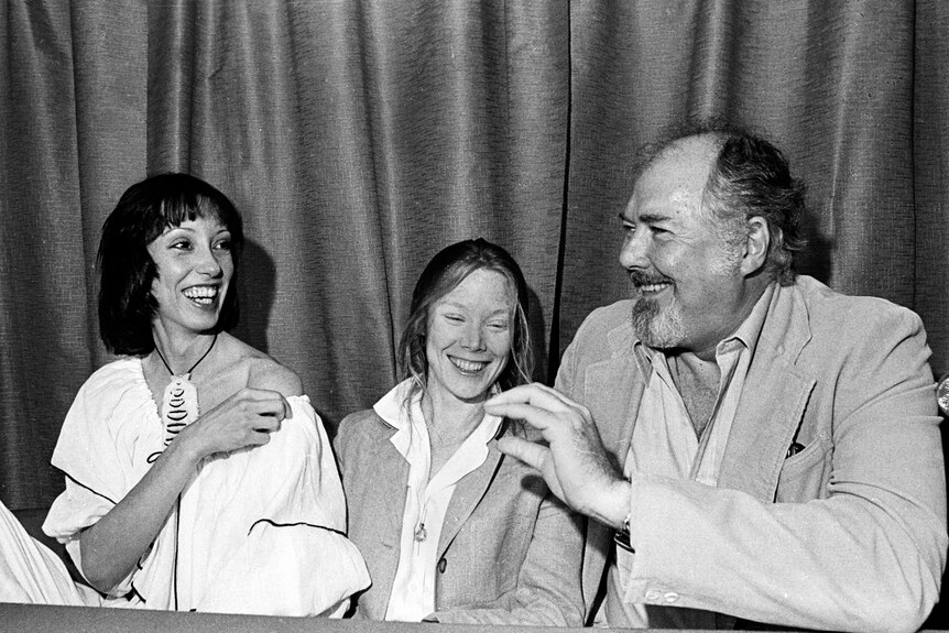 Shelley Duvall, Sissy Spacek and Robert Altman sit at a table, laughing. 
