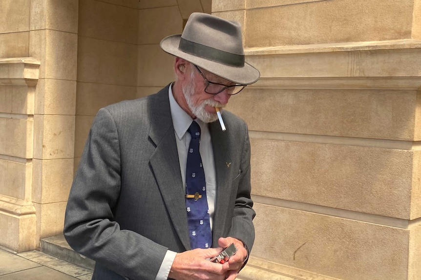 An elderly man in a trilby hat walks past a building.