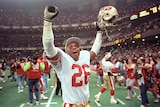 An American footballer puts his arms in the air in victory while holding his helmet at the Super Bowl.
