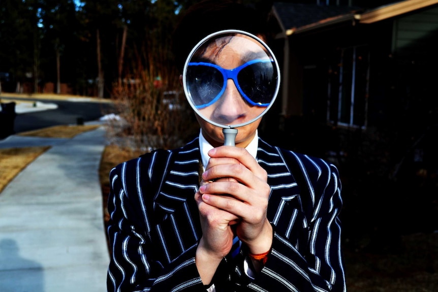 A person holds a magnifying glass to depict techniques to help you overcome imposter syndrome.