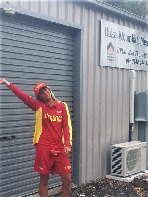 Young girl in yellow and red lifeguard uniform outside surf-lifesaving club shed in Iluka, NSW
