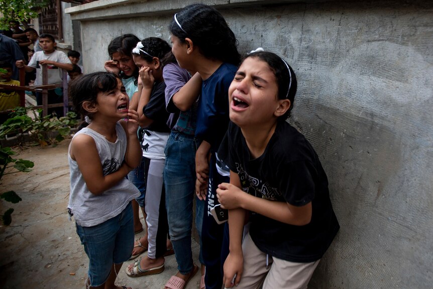 A group of children cry uncontrollably near a wall during a Palestinian funeral.