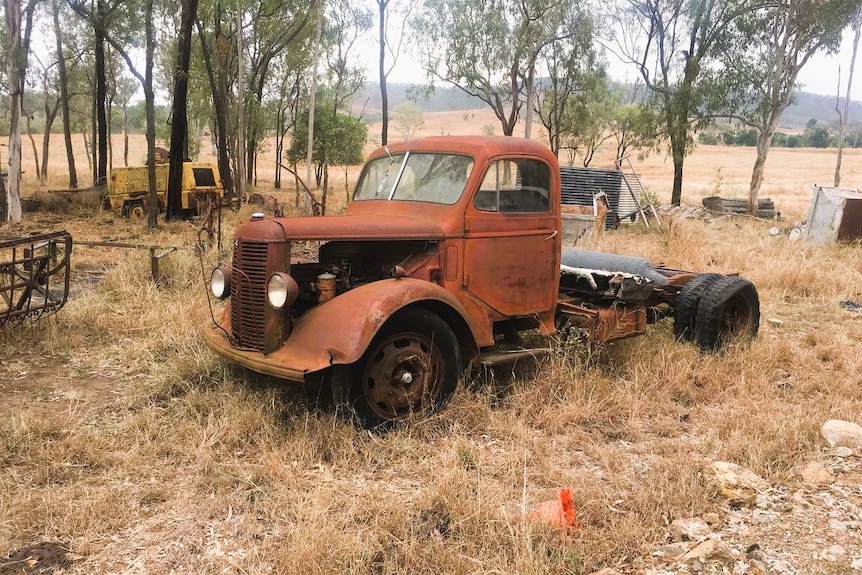 A rusty truck parked up on a rural property.