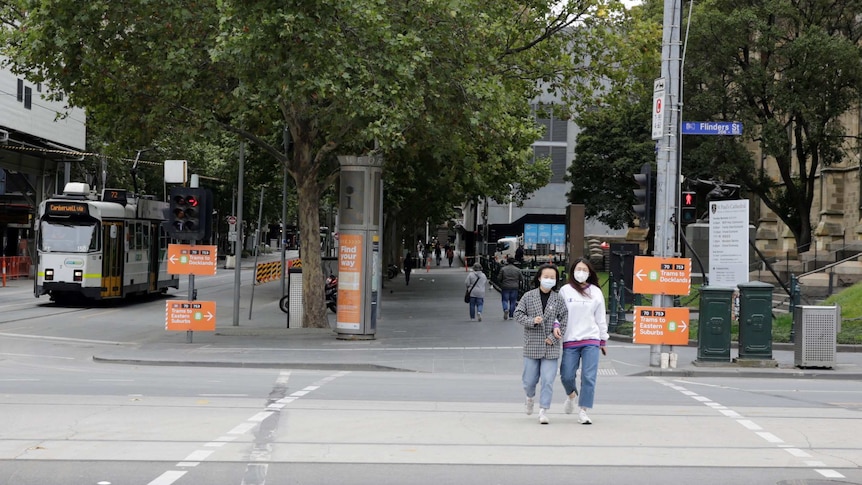 People wear masks while walking near a tram.