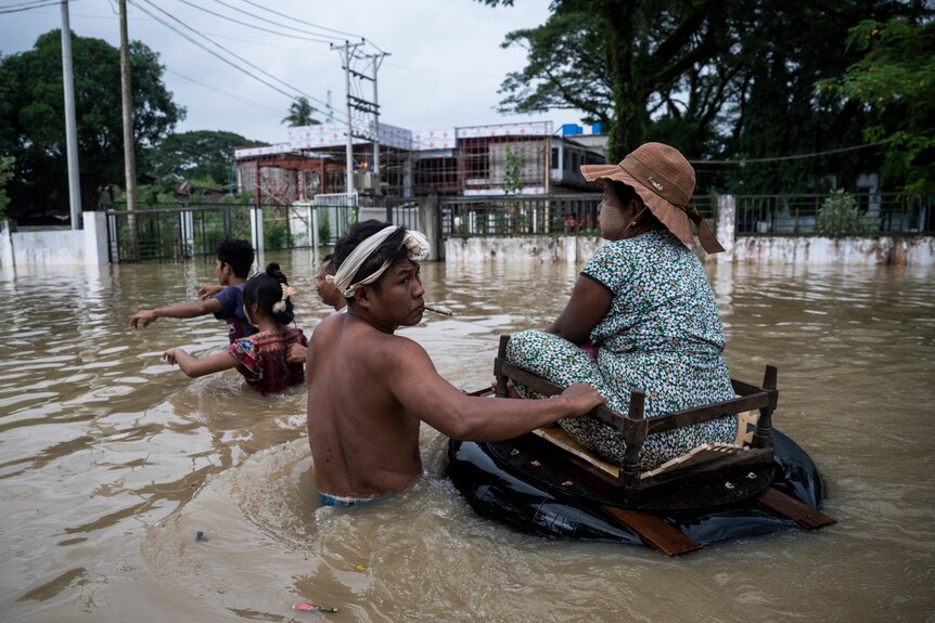 A man pushes a woman floating on an inner tube through flood waters. 