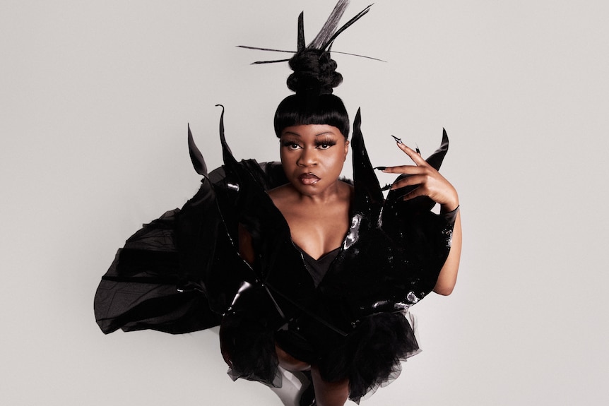 A 2022 press shot of Sampa The Great dressed in spiky black dress with matching hair against beige background