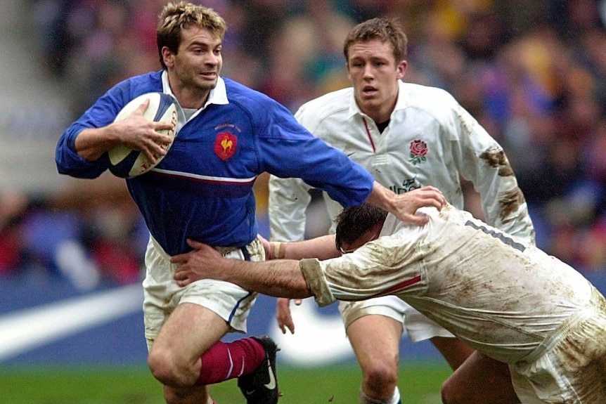 Christophe Dominici fends off a tackler who is trying to grab him by the waist