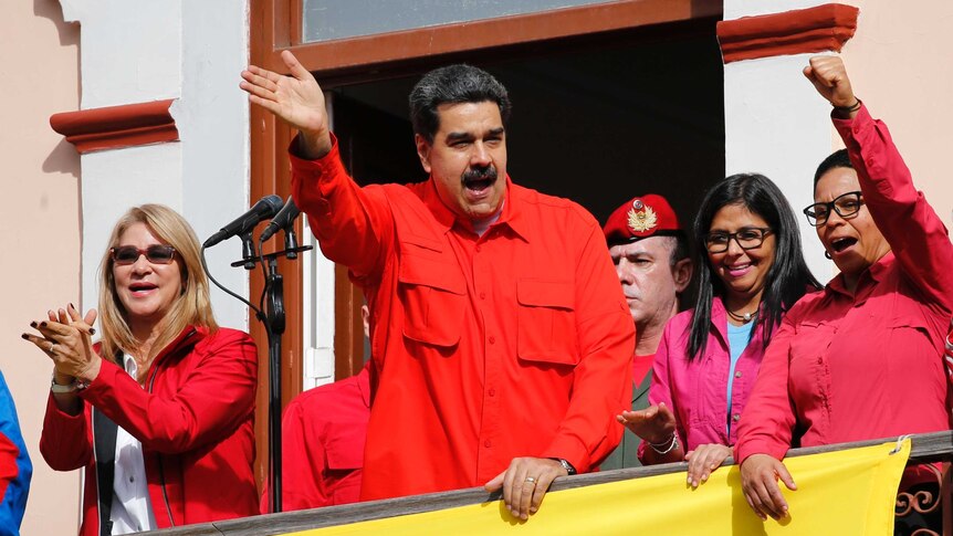 Venezuela's President Nicolas Maduro and first lady Cilia Flores, both dressed in red, interact with supporters from a balcony.