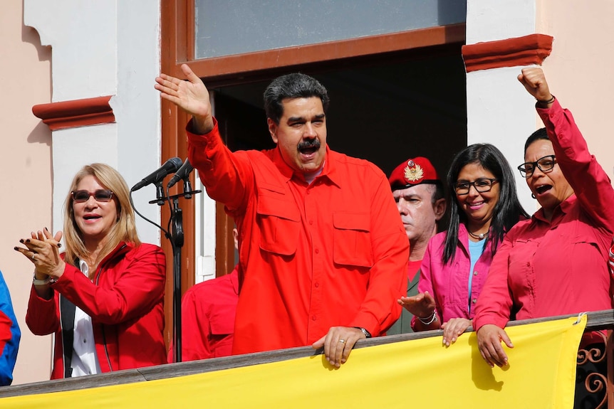 Venezuela's President Nicolas Maduro and first lady Cilia Flores, both dressed in red, interact with supporters from a balcony.