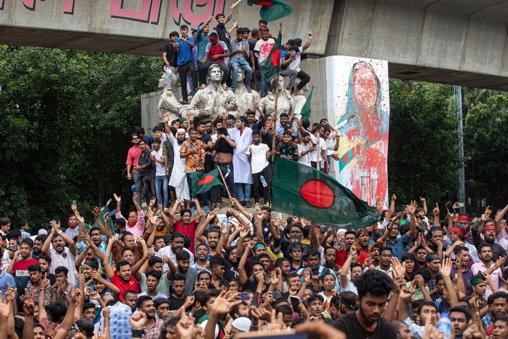 Large group of people gather under a bridge with a flag and grafitti of woman