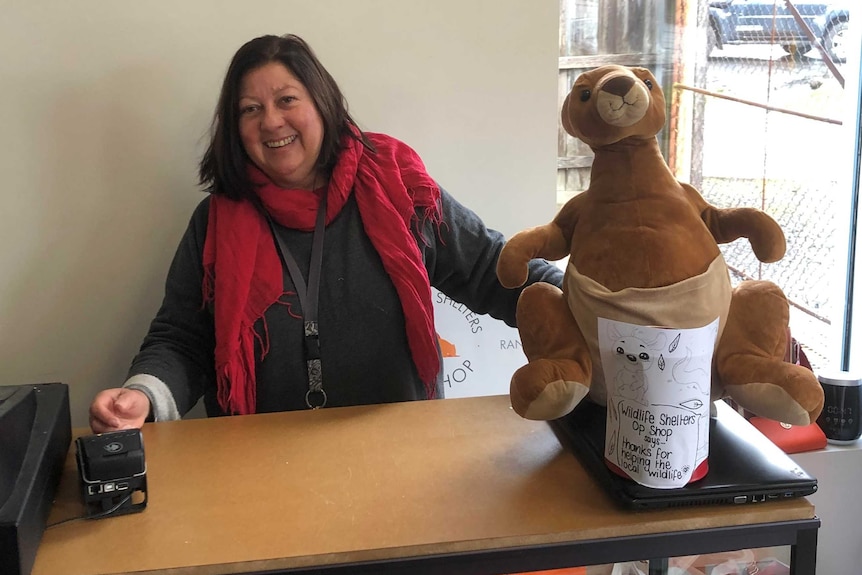 A lady with a red scarf is sitting at a table with a brown toy bear next to her