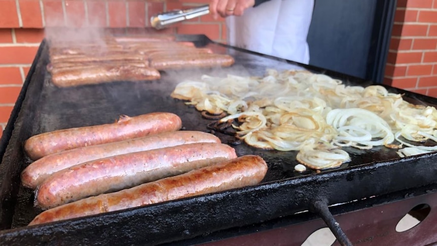 Sausages and onion cooking on a barbecue.