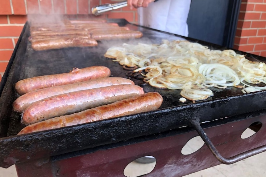 Sausages and onion cooking on a barbecue.