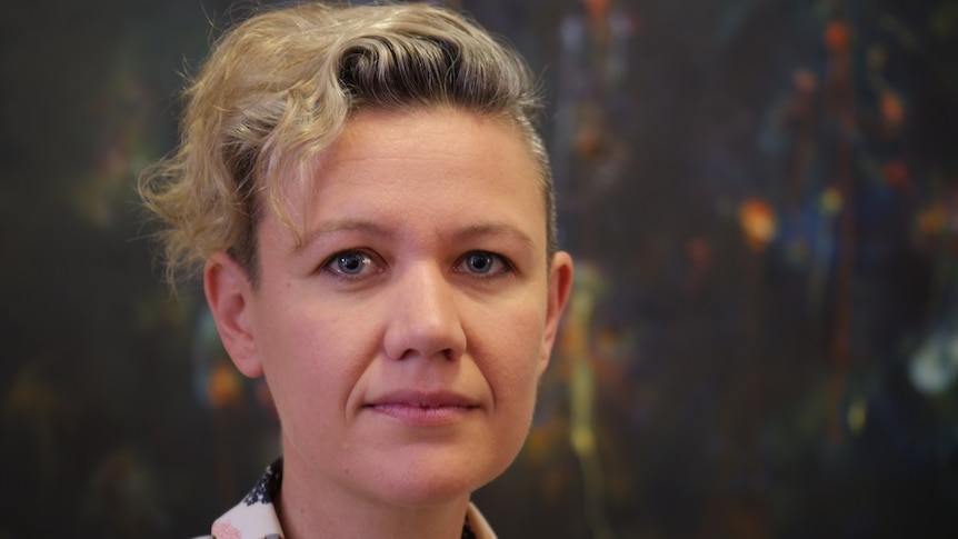 A woman with short, curly blonde hair stares at the camera.